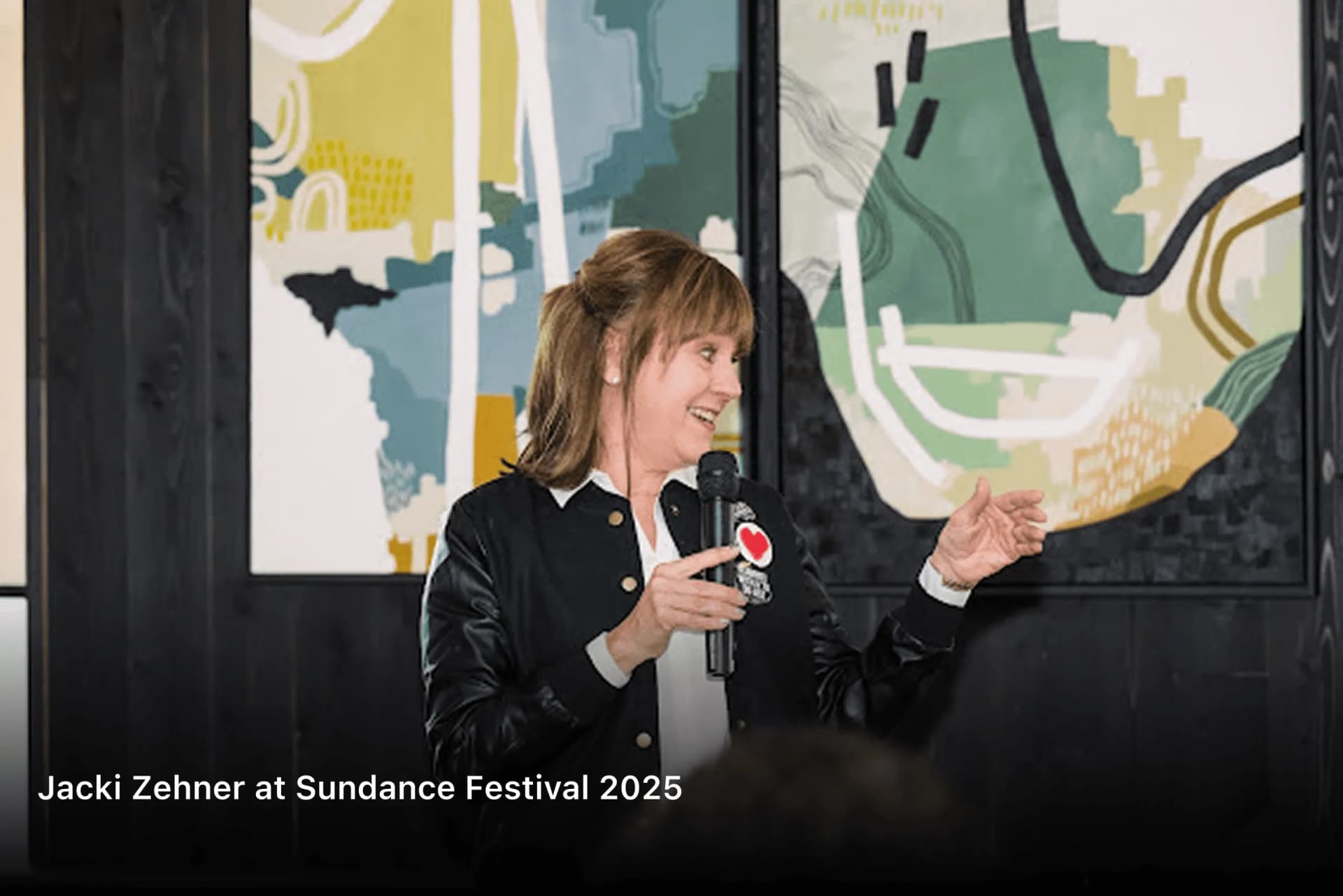 Jacki Zehner speaking with a microphone in front of abstract artwork at Sundance Festival 2025