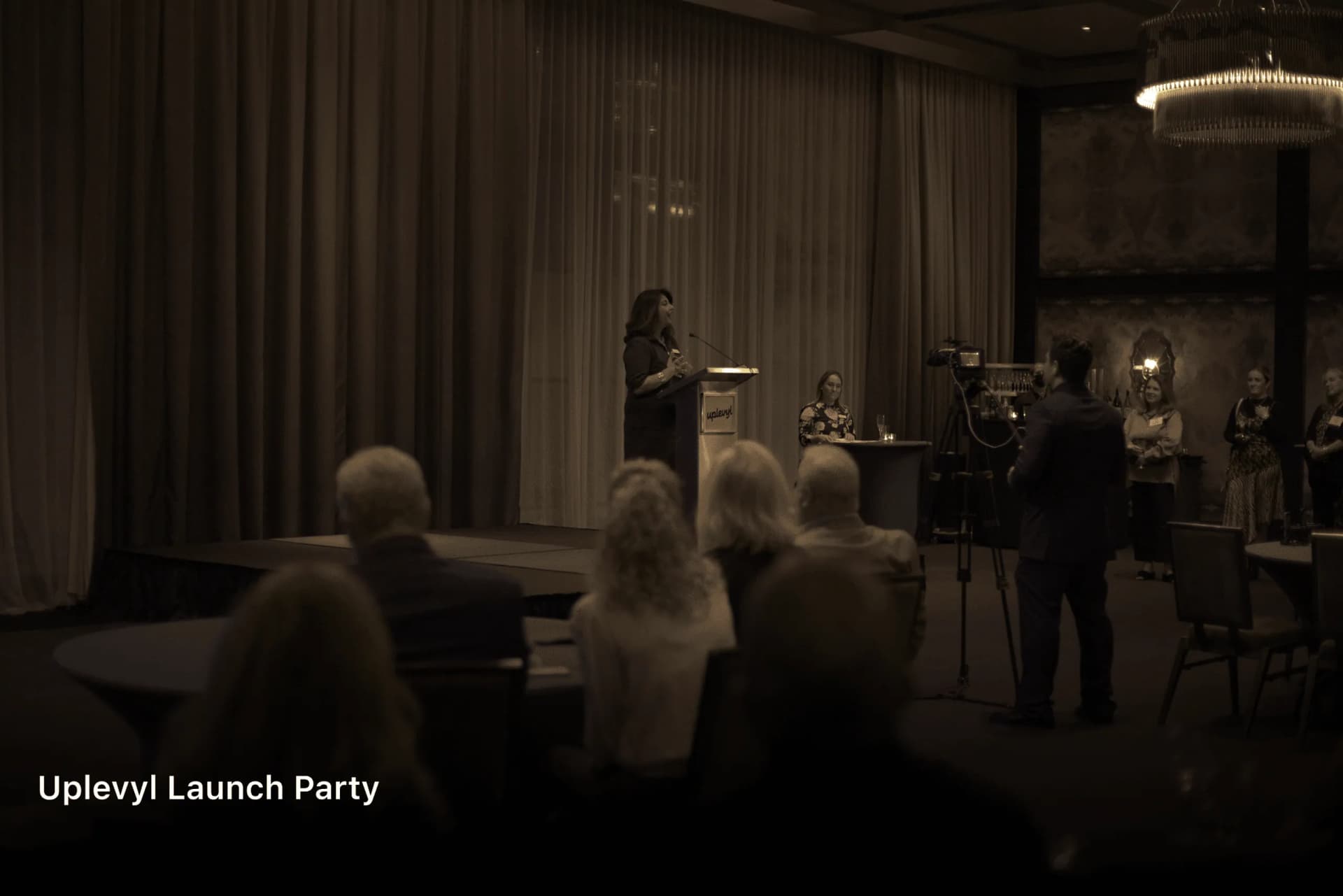 Shubhi Rao speaking at a lectern to a seated audience at the Uplevyl launch party